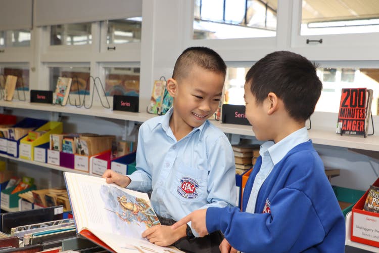 Two students enjoying sharing a picture book in the school library.