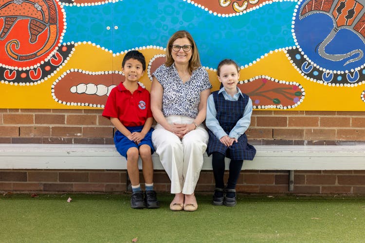 The Normanhurst Public School principal sitting with two students in front of a colourful Indigenous mural.