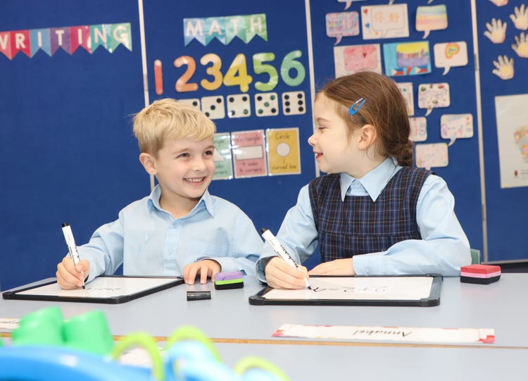 Two students in a colourful classroom working on whiteboards.