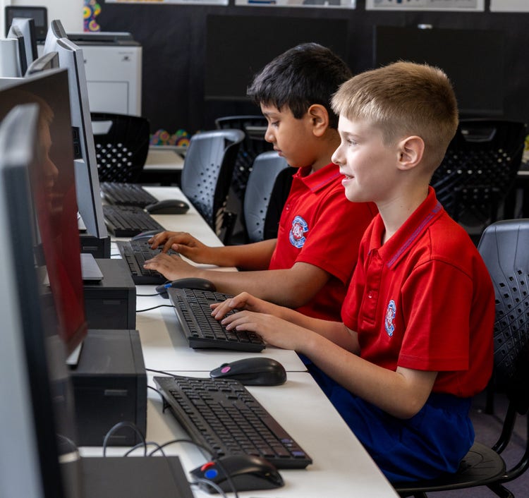 Two students working on desktop computers in the school technology lab.